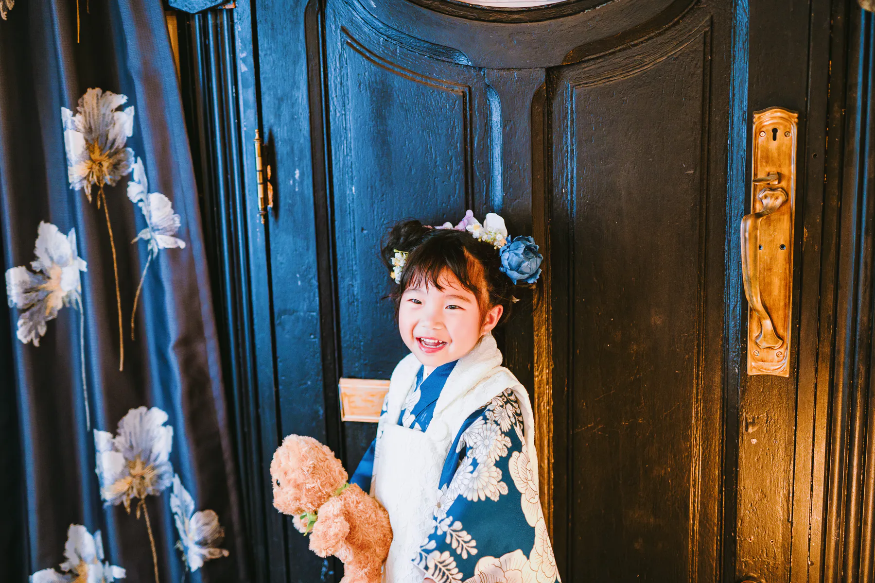 黒い扉の前でくまを抱えて笑う、青い着物の子ども