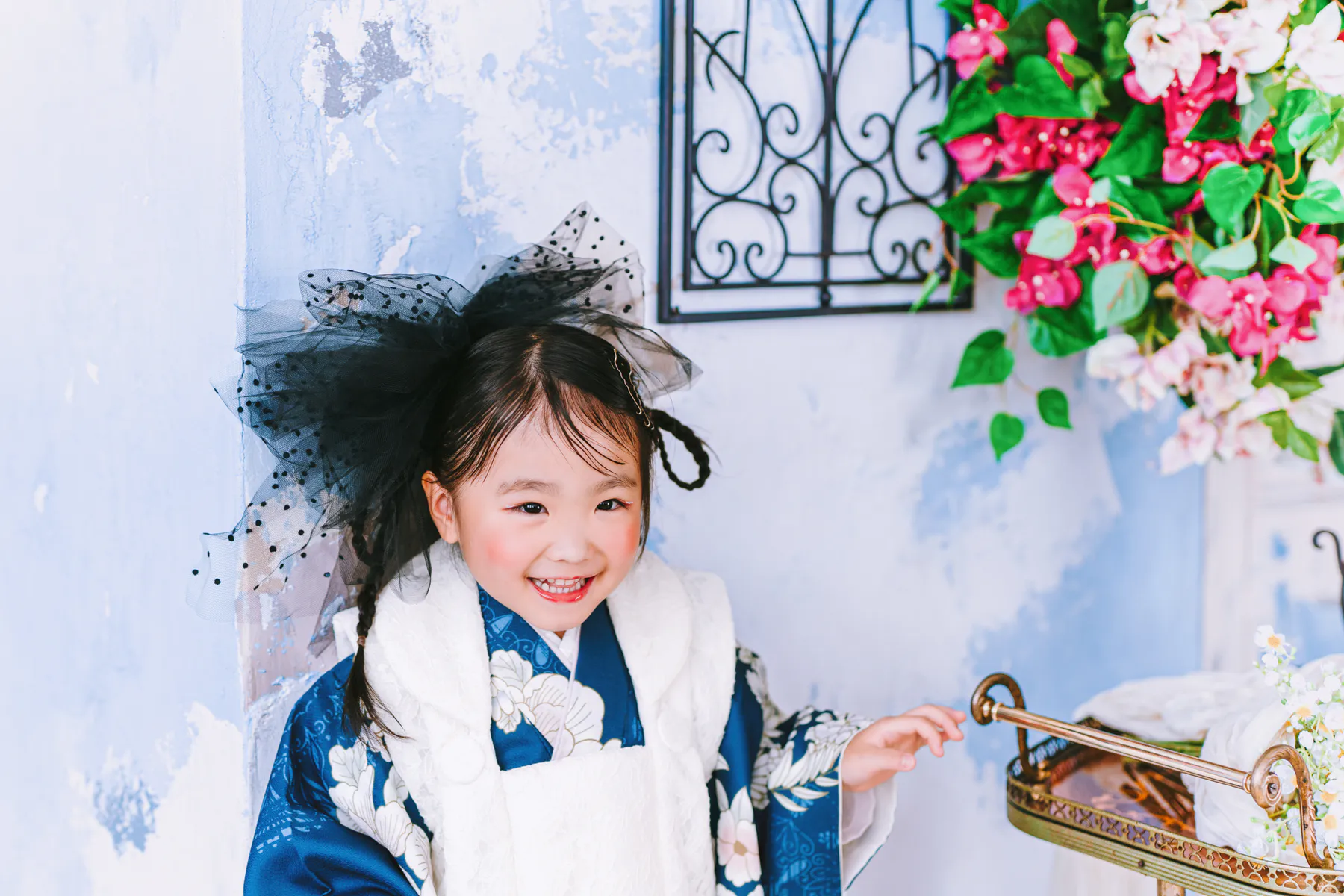 花の壁の前で笑う、青い着物の子ども
