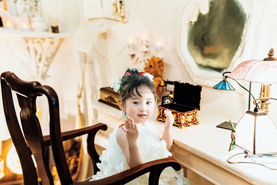 鏡のある部屋の椅子に座る、白いドレスの子ども